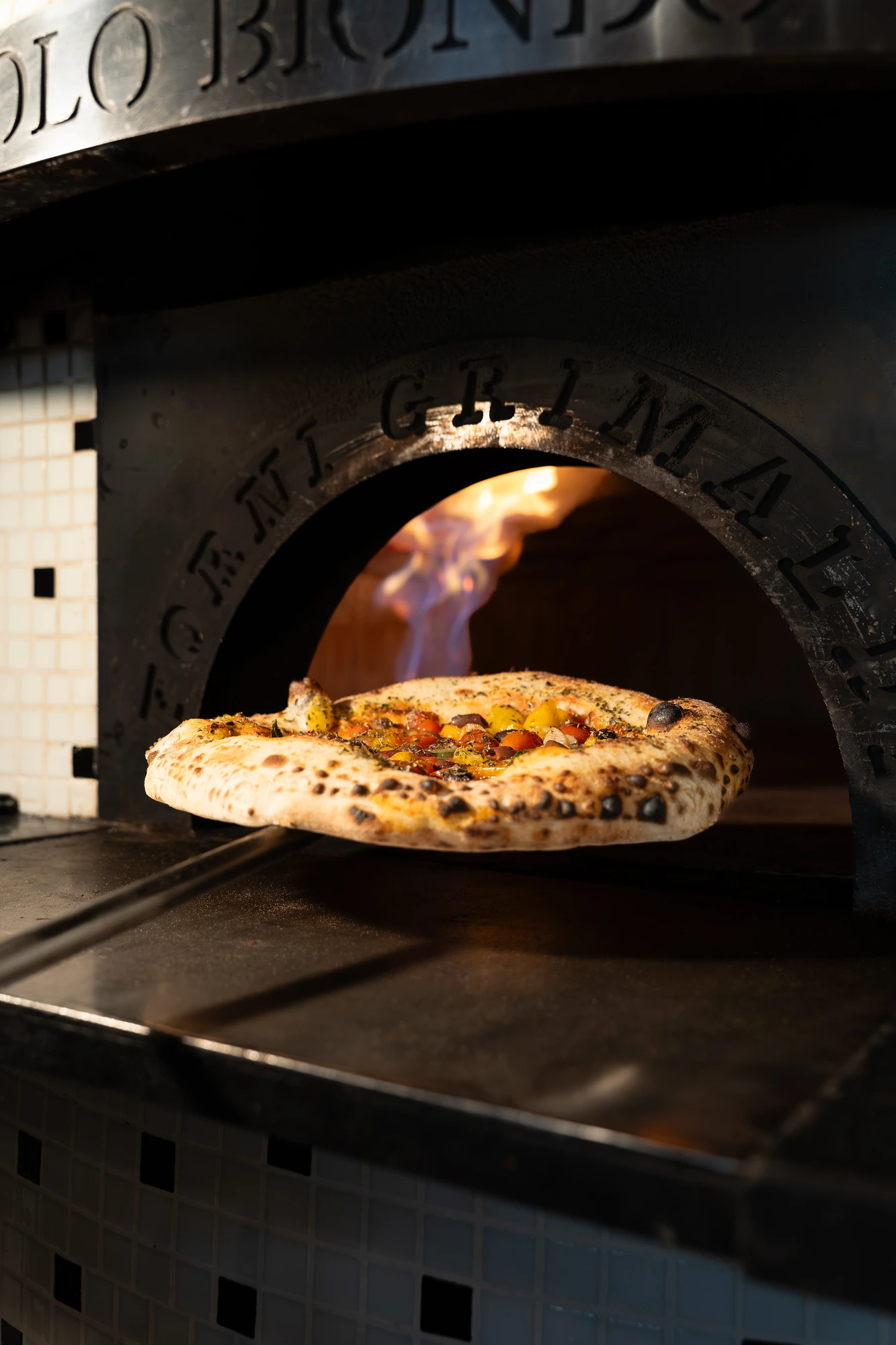 Pizza napolitana saliendo del horno de leña con llama viva